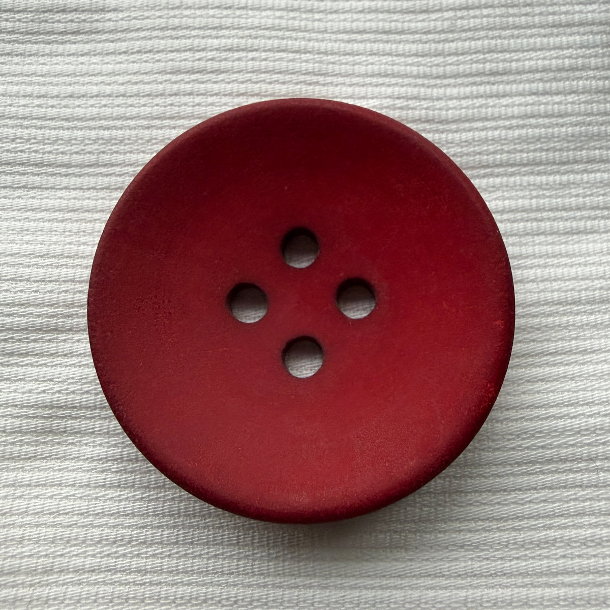 Red casein four-hole button on white fabric, deepening in colour toward the rim.