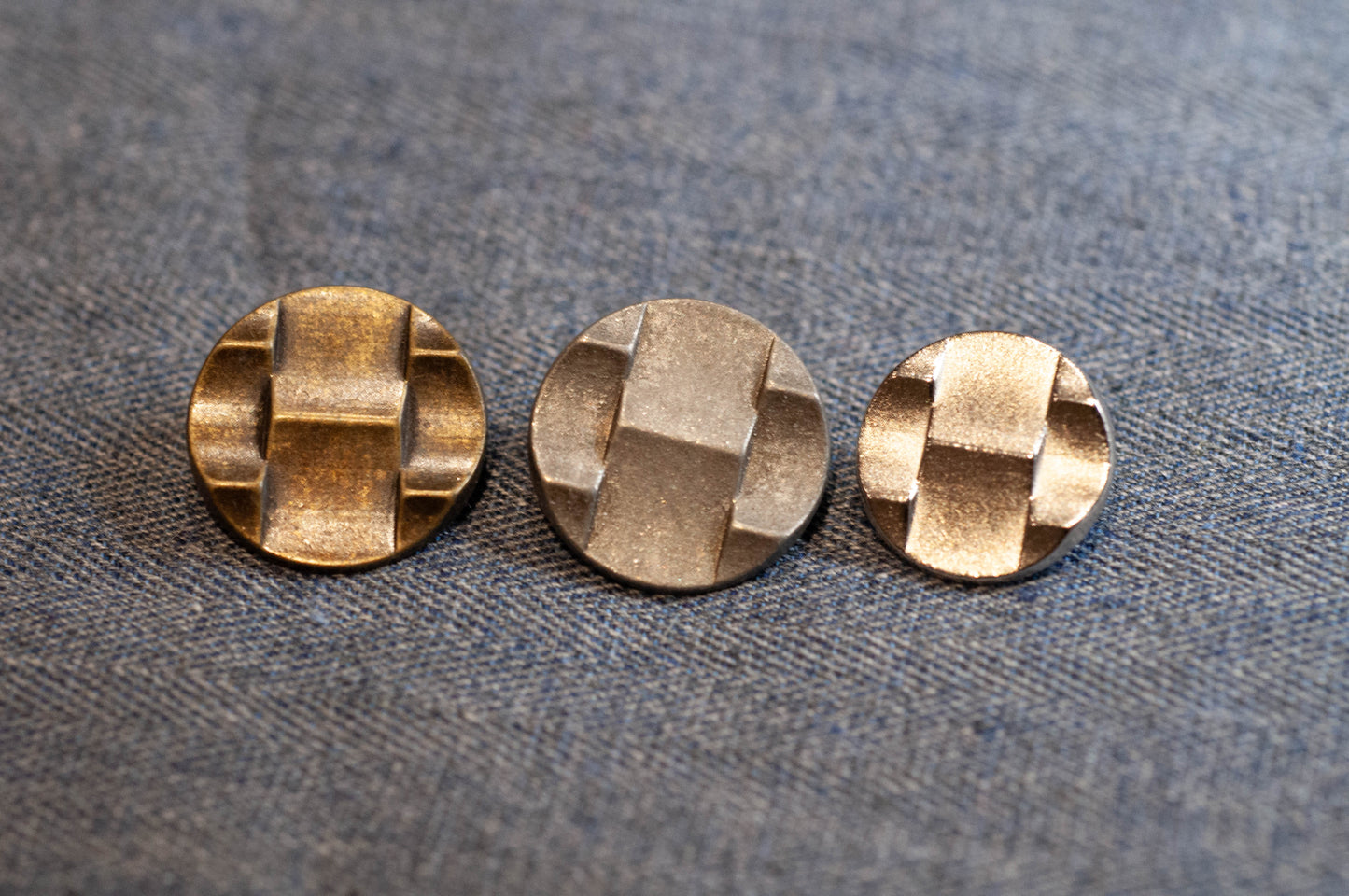 Three metallic buttons with a geometric pattern on a textured fabric background