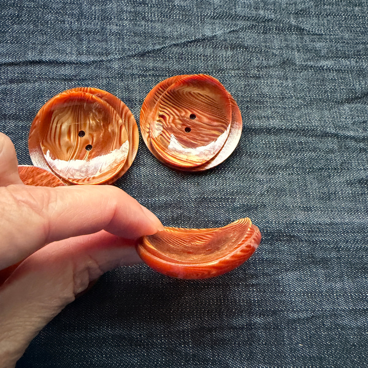 Hand holding a rust swirl button to show its curled side profile.