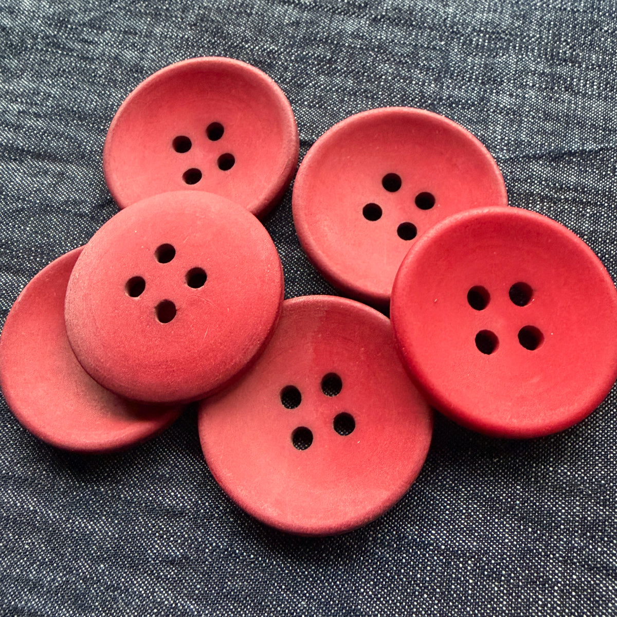 Matte red casein buttons with a gently dished centre, stacked on denim.