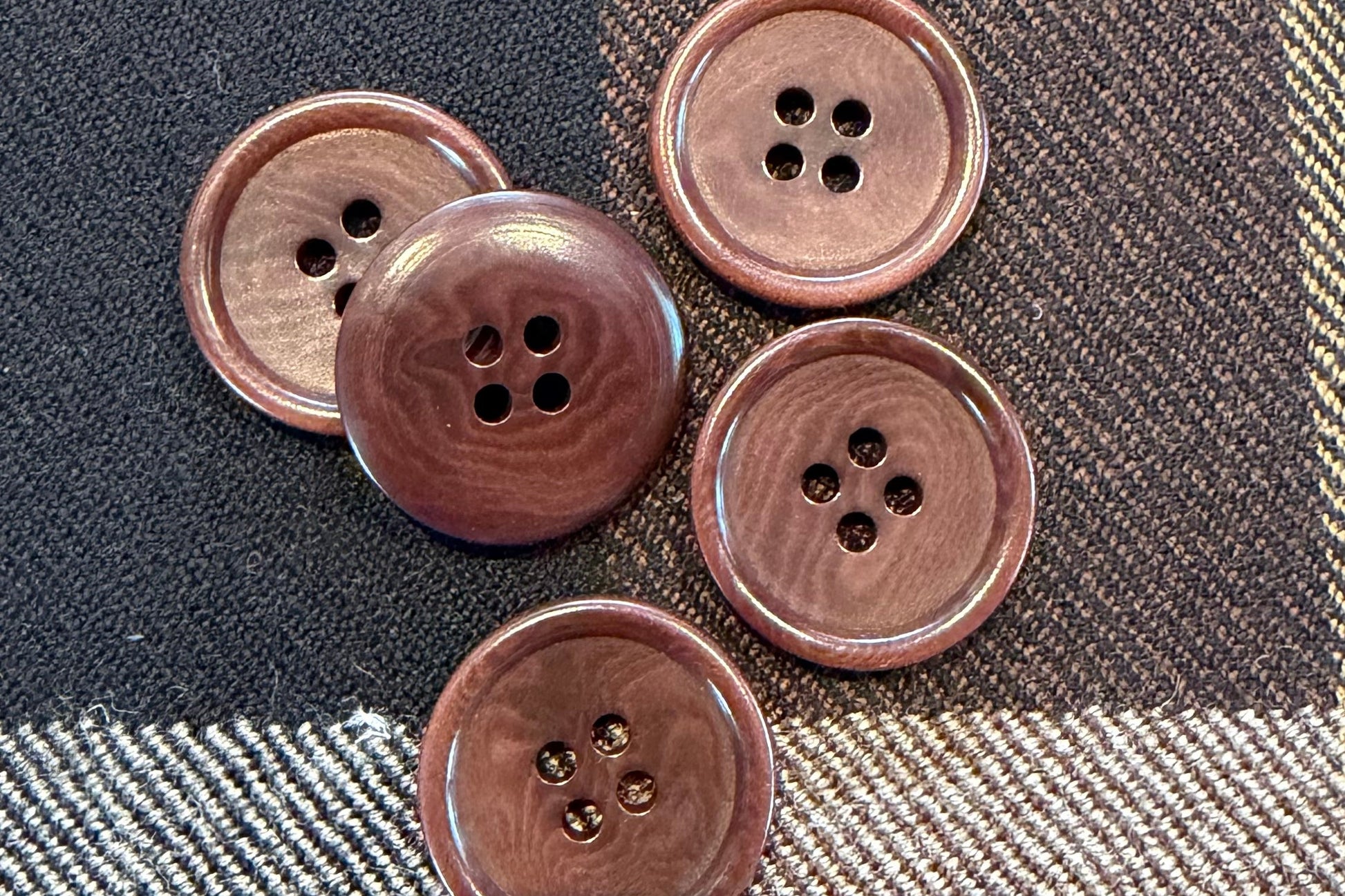 Five brown buttons on plaid fabric.