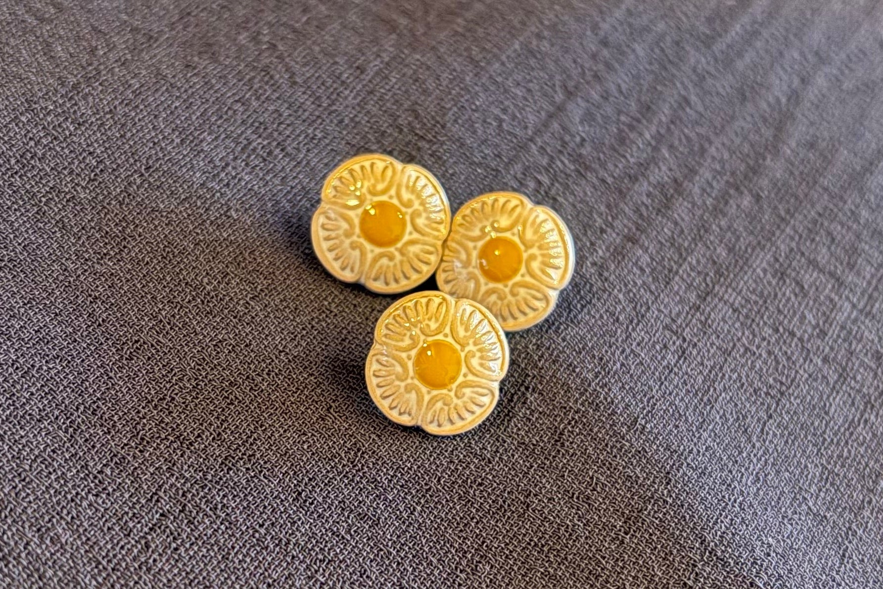 Three yellow flower buttons on a textured gray fabric background