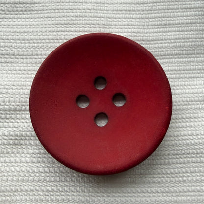 Red casein four-hole button on white fabric, deepening in colour toward the rim.