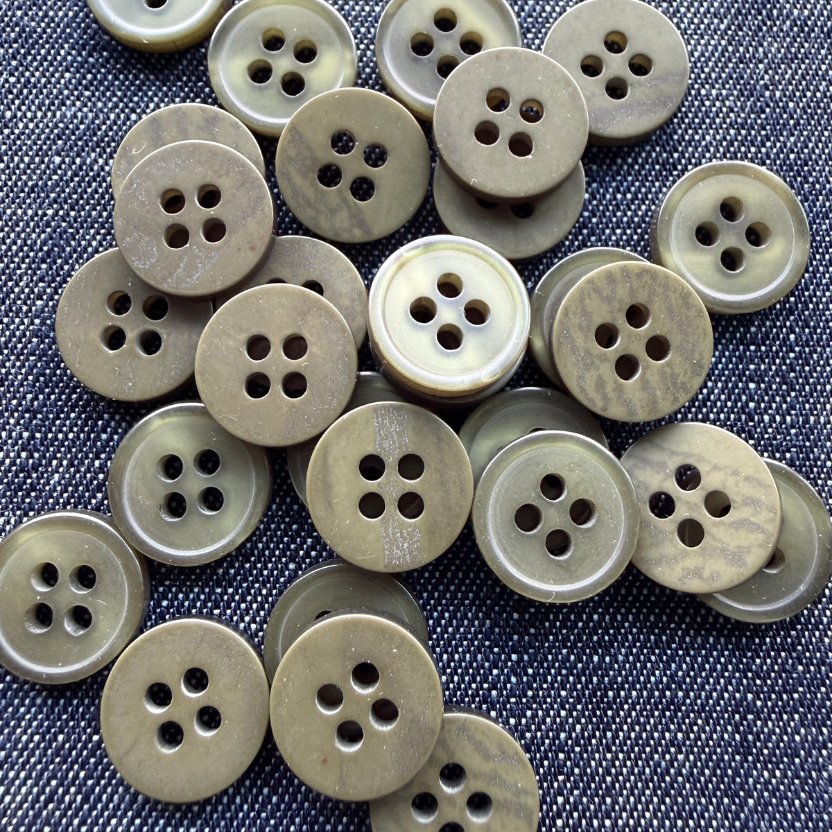 Glossy olive four-hole plastic shirt buttons on denim