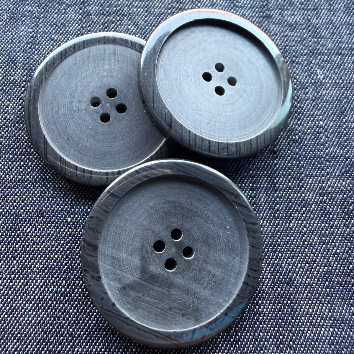 Large black four-hole plastic coat buttons on denim