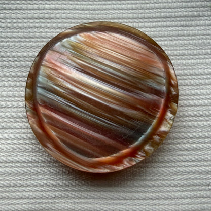 Rose-gold casein statement button in deeper bronze tones on a white textured fabric.