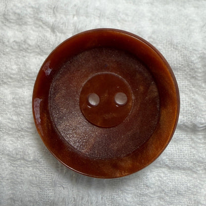 A single round brown button with two holes, photographed from above on a textured white fabric background.