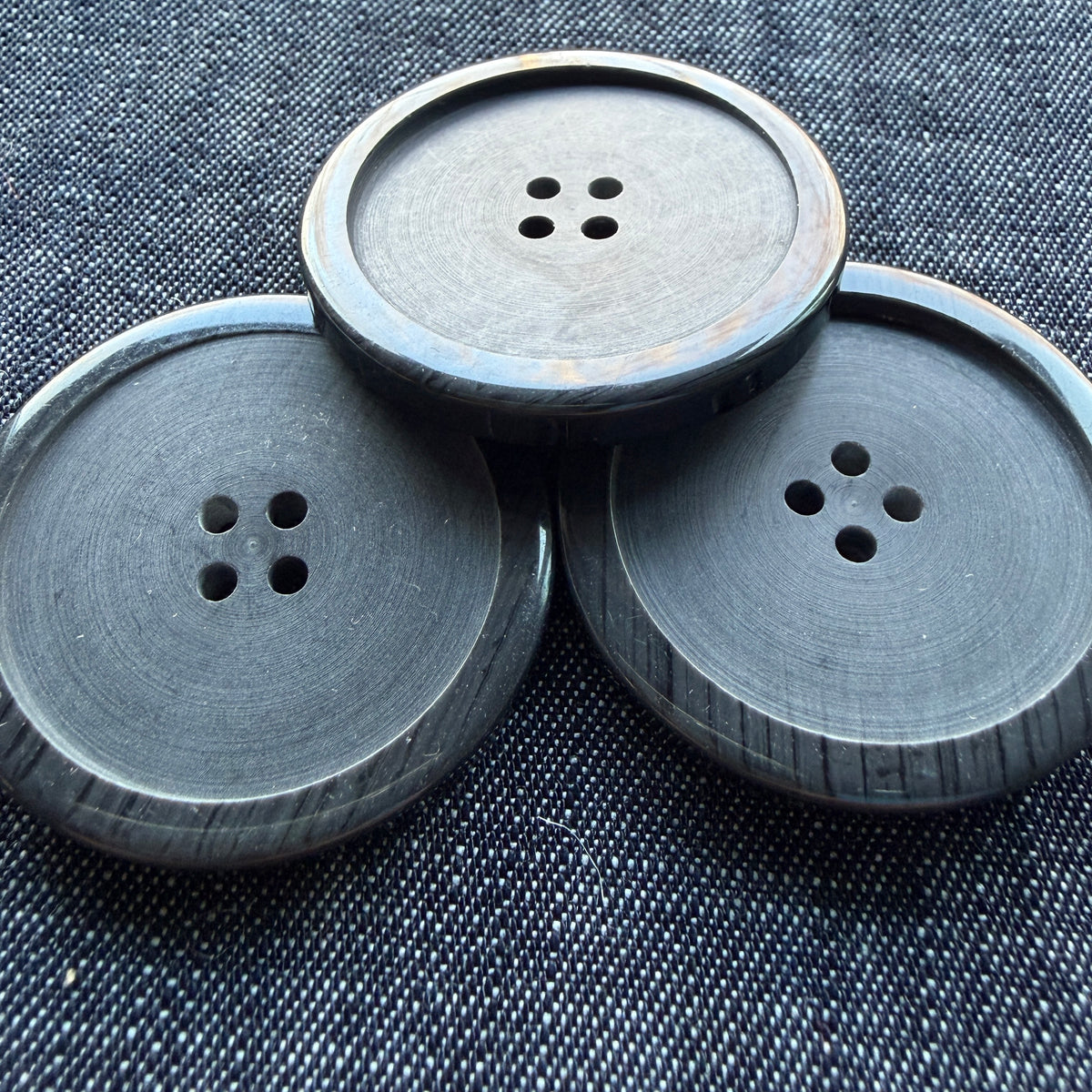 Three large soft black four-hole plastic coat buttons on denim