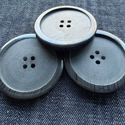 Three large soft black four-hole plastic coat buttons on denim