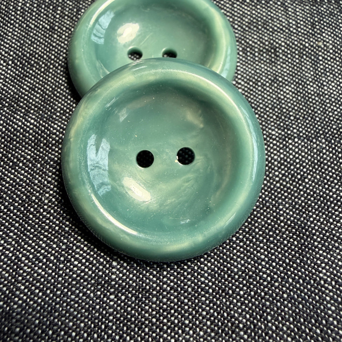 Polished teal casein two-hole button with a concave centre.