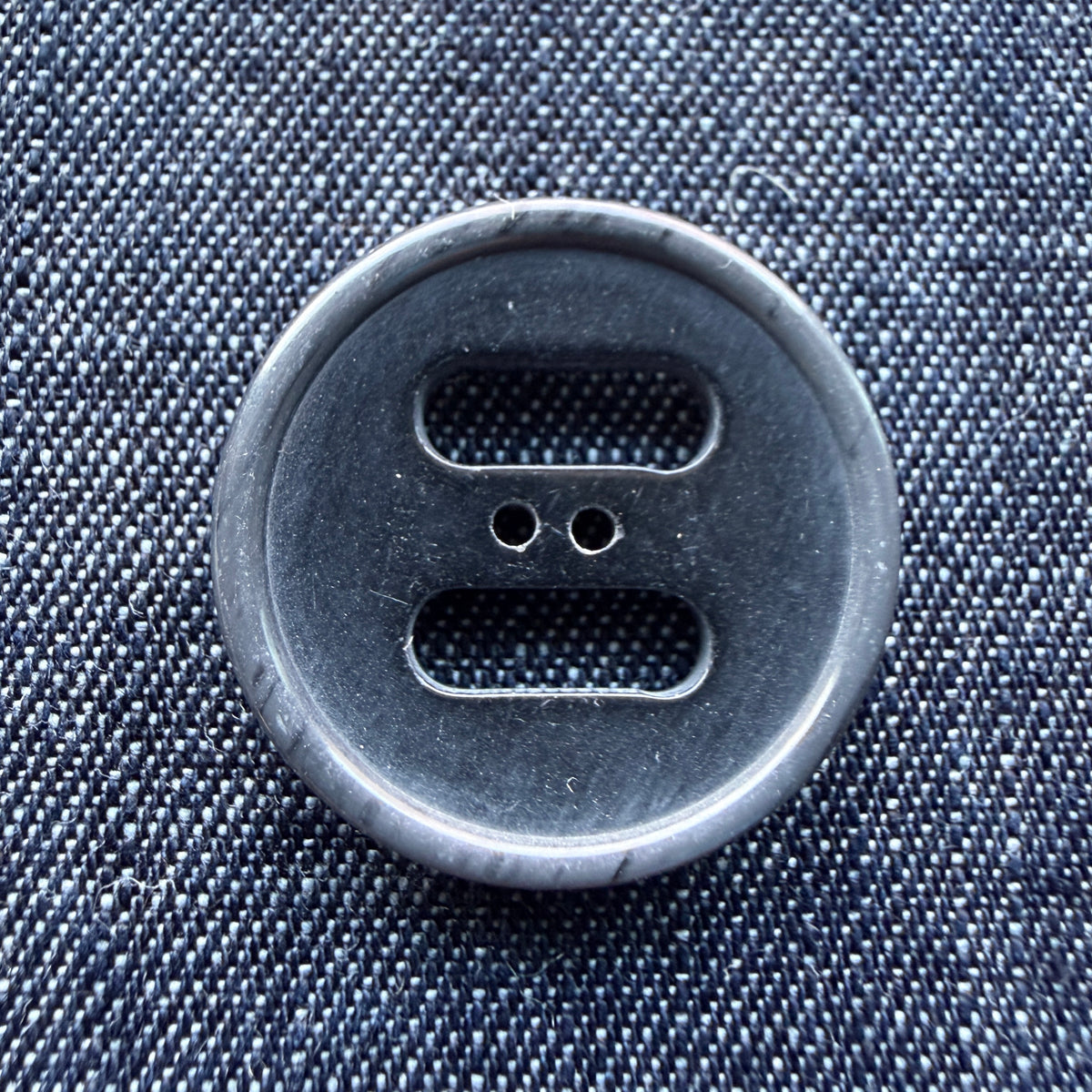 Close-up of a grey slotted plastic coat button on denim