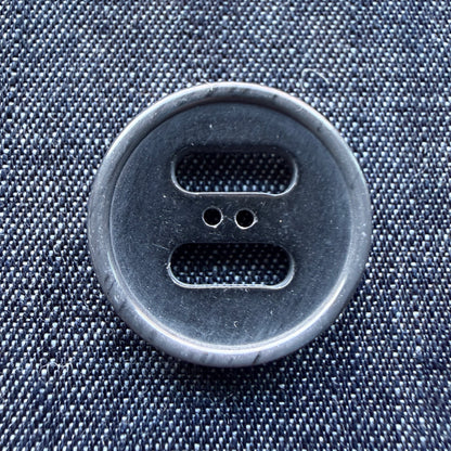 Close-up of a grey slotted plastic coat button on denim