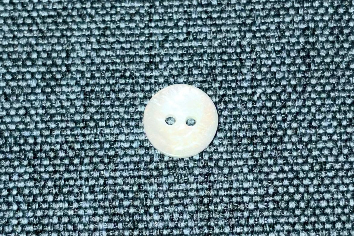 Close-up of a white button on textured blue fabric.