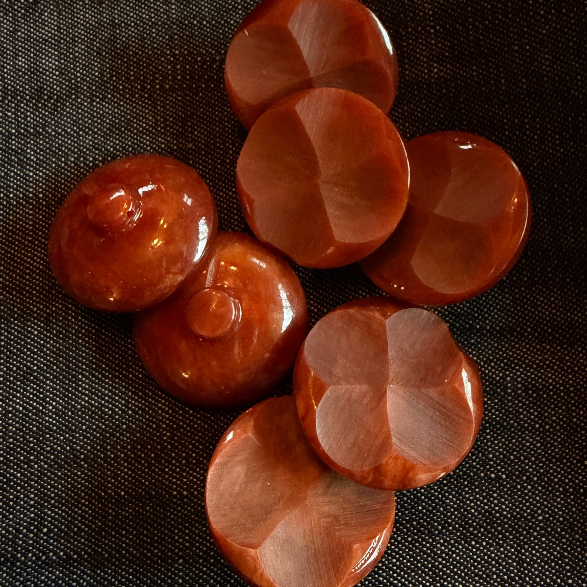 Six polished reddish-brown buttons arranged on a dark textured fabric background.