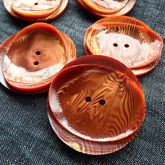 Rust and copper statement buttons with a wood-like swirl and a curled, rolled lip.