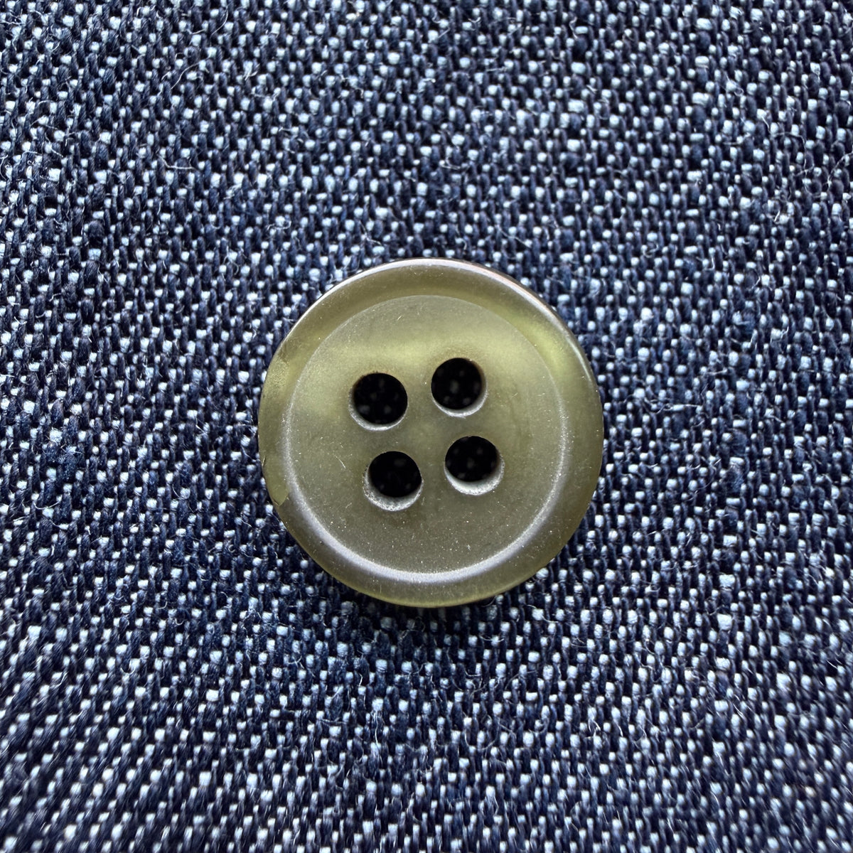 Glossy olive four-hole plastic shirt buttons on denim