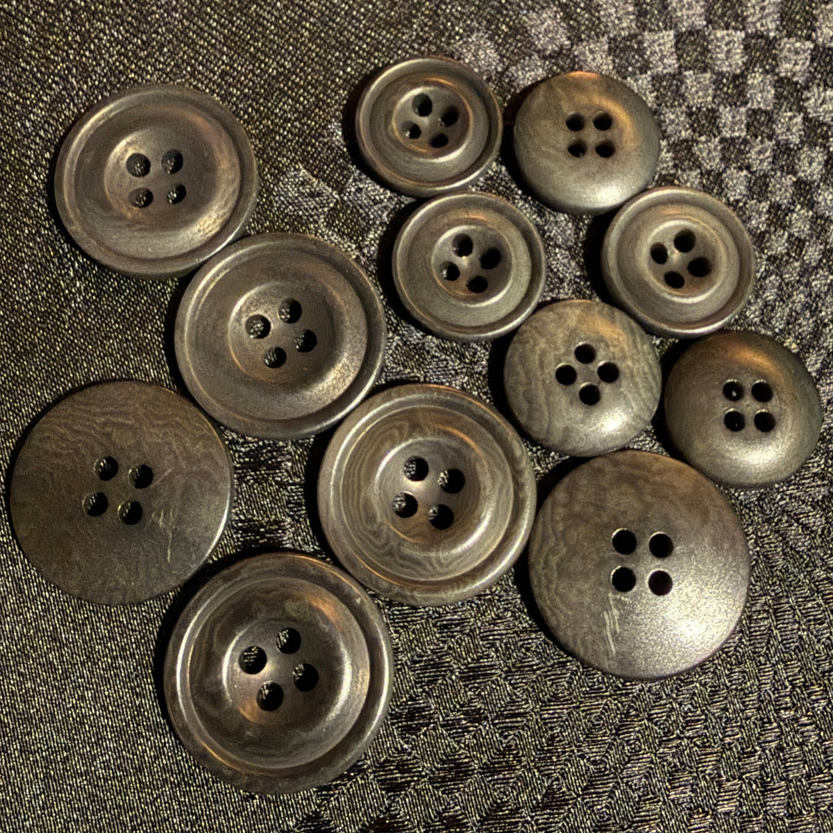 A group of ten buttons, arranged on a dark textured fabric background.