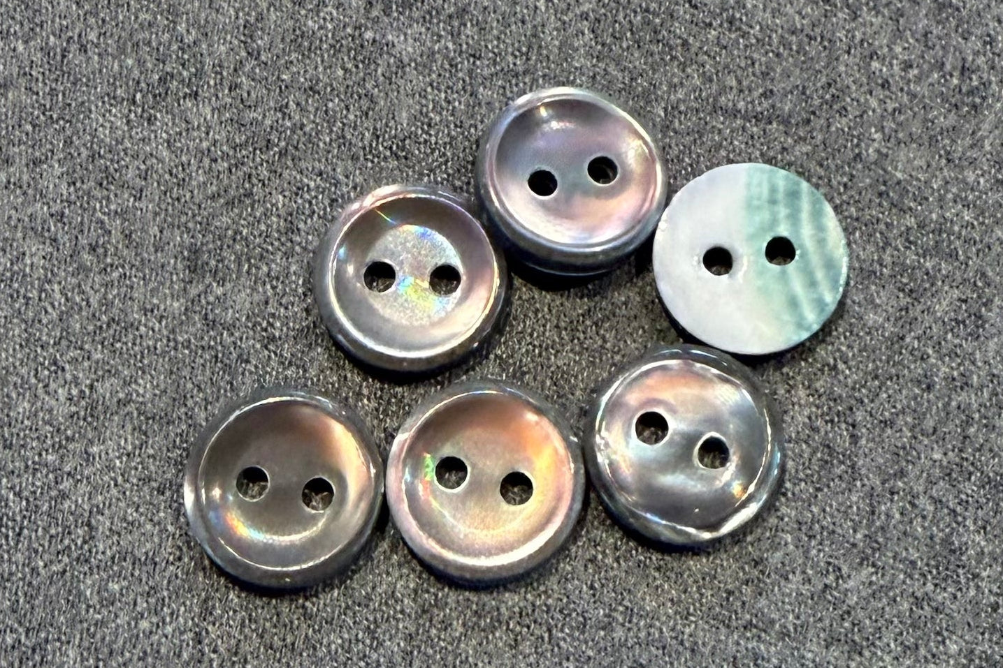 Set of six pearly grey buttons on a gray fabric surface