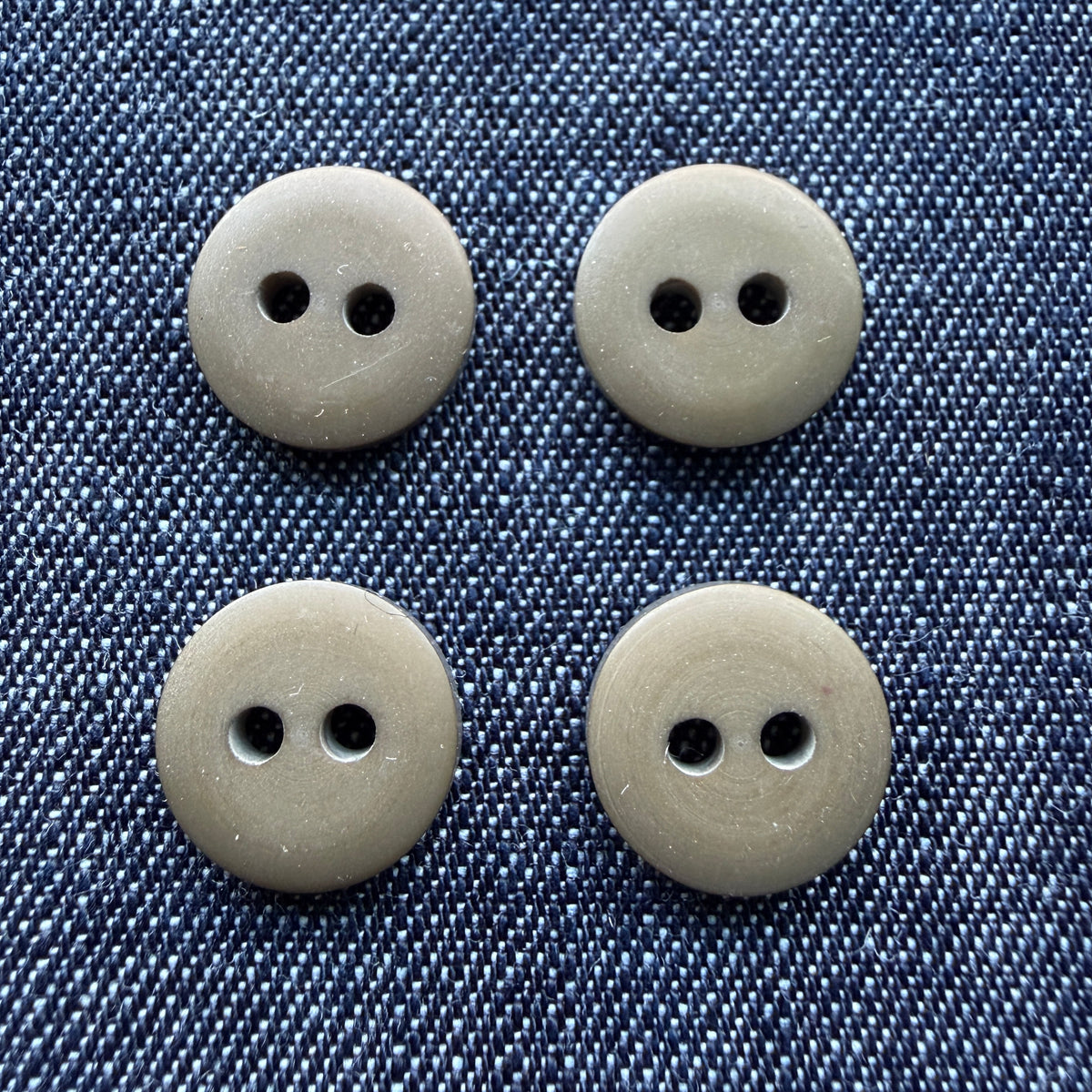 Four matte olive two-hole plastic shirt buttons on denim