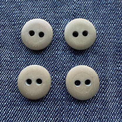 Four matte olive two-hole plastic shirt buttons on denim