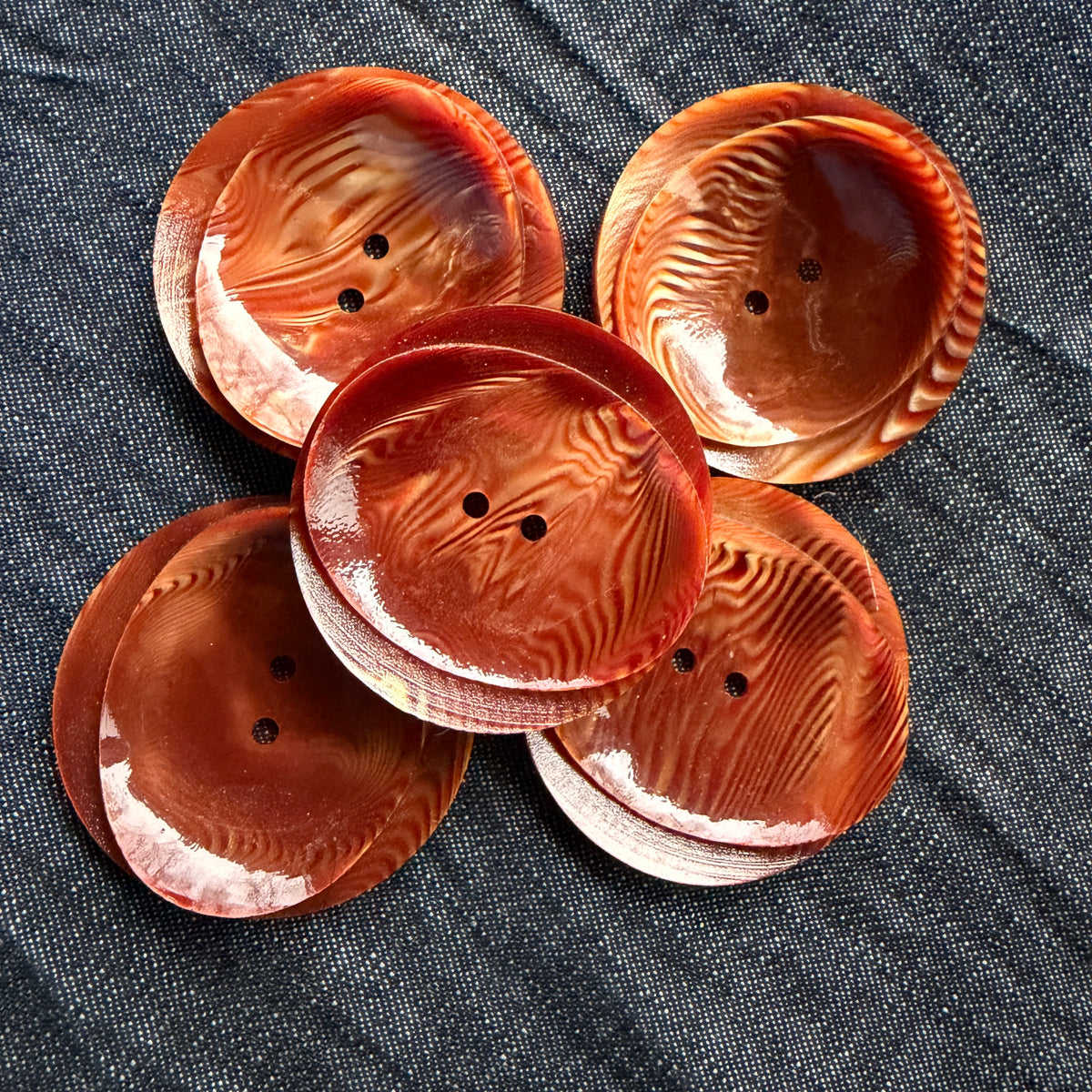 A group of rust swirl buttons in 42 mm and 48 mm sizes on denim.