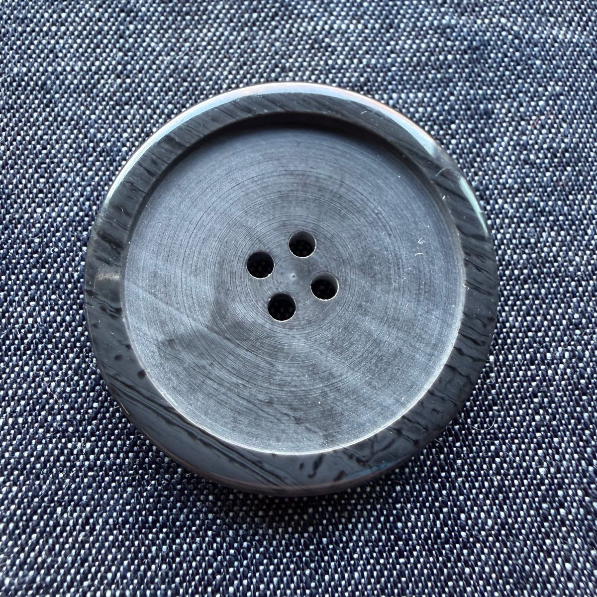 Close-up of a large black plastic coat button with a streaked, distressed rim