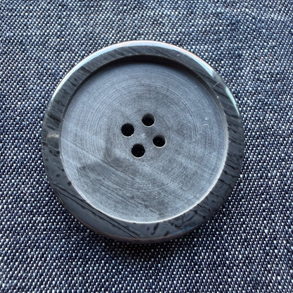 Close-up of a large black plastic coat button with a streaked, distressed rim