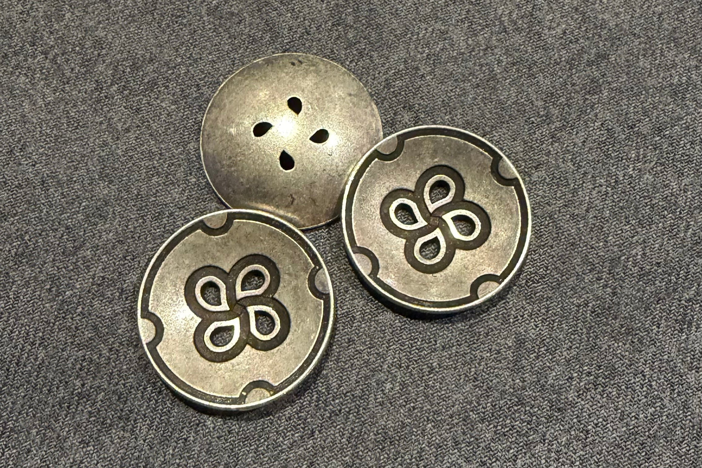 Three metallic buttons with floral designs on a textured surface