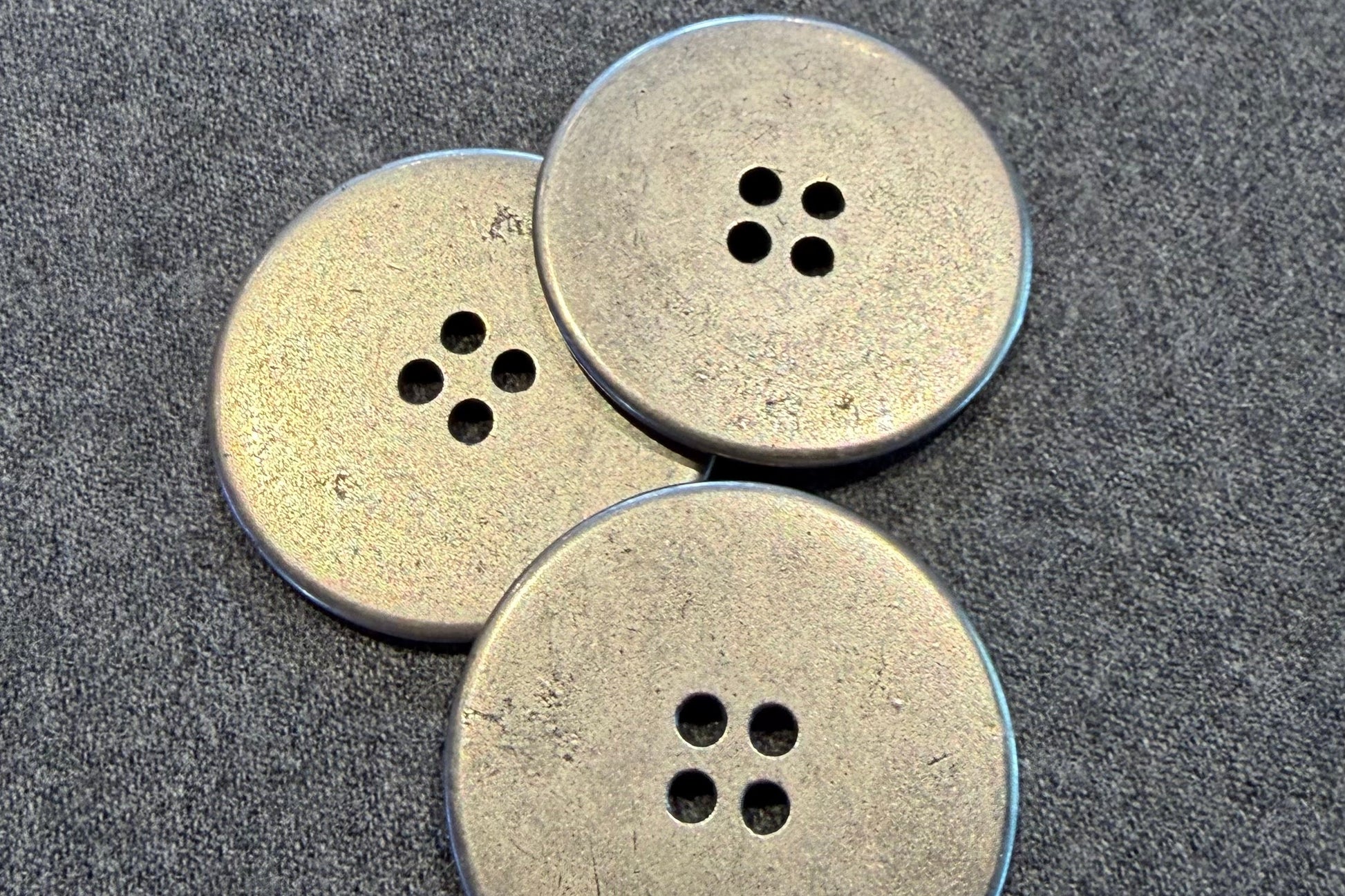Three silver buttons with four holes on a textured surface