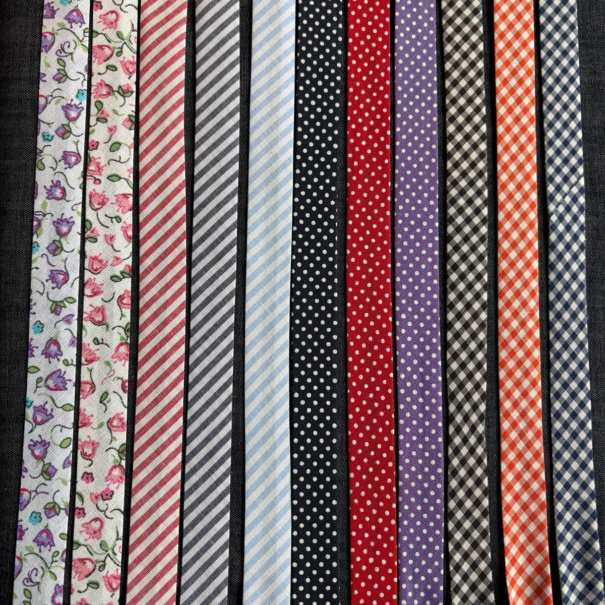 Eleven patterns of cotton bias tape laid side by side: florals, stripes, polka dots and gingham