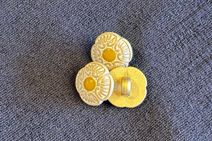 Three decorative buttons with floral patterns on a textured surface