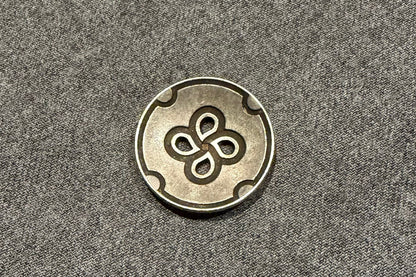 Metallic button with a four-leaf clover design on a gray fabric background