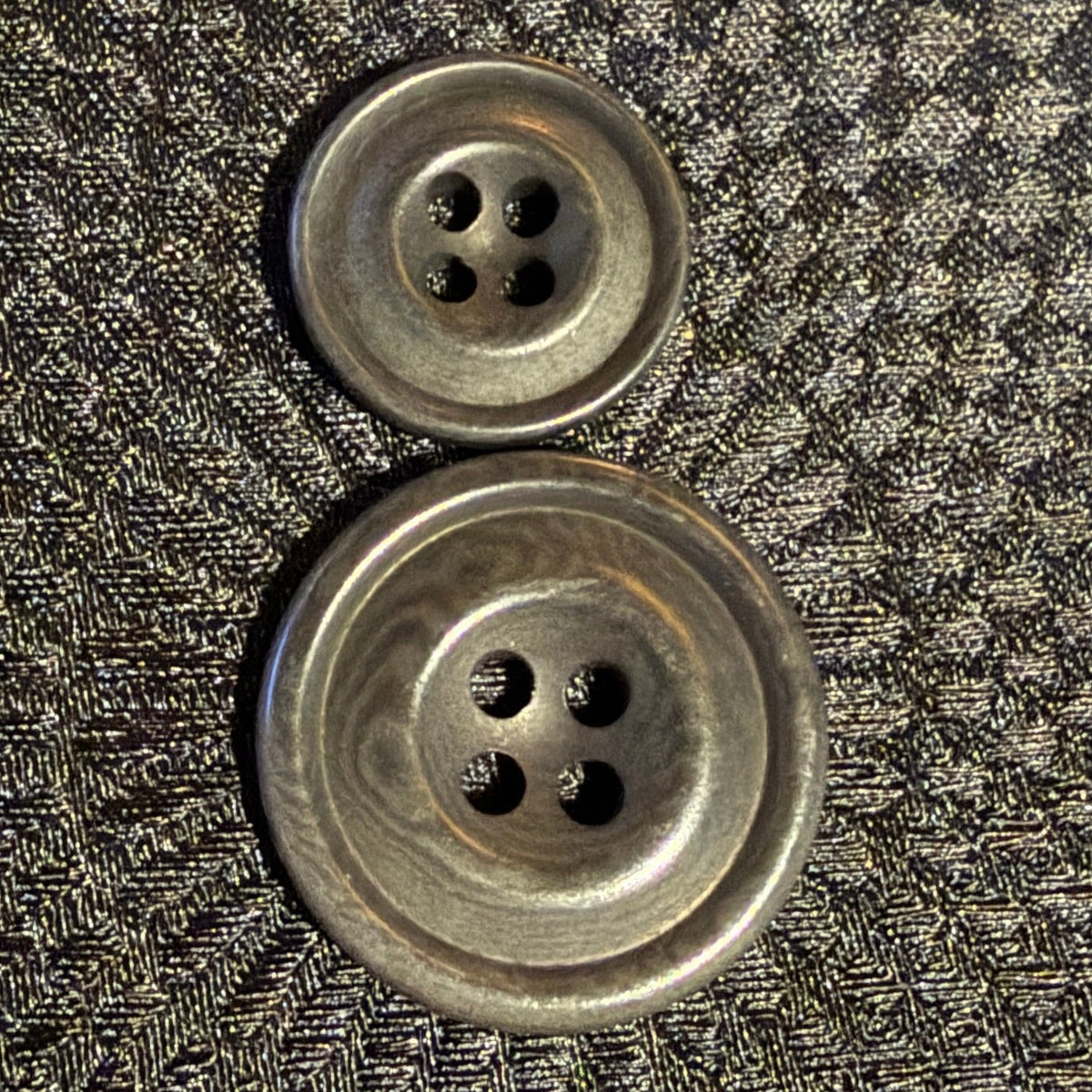 Two grey buttons made of corozo in two sizes, each with four holes.