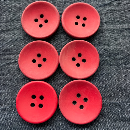 Set of six matte red casein four-hole buttons on denim.