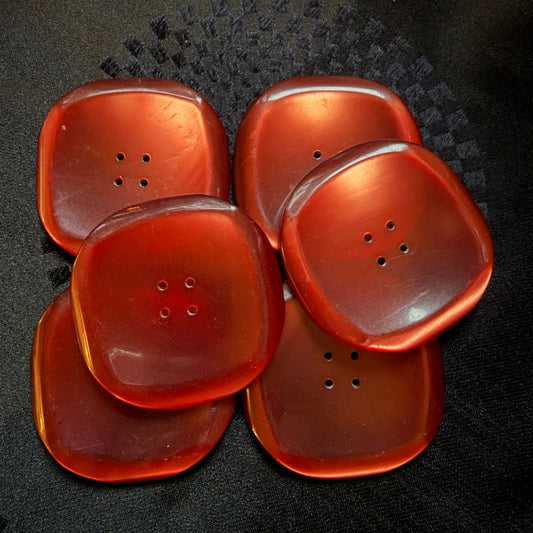 Six square red glass buttons with four holes on black fabric