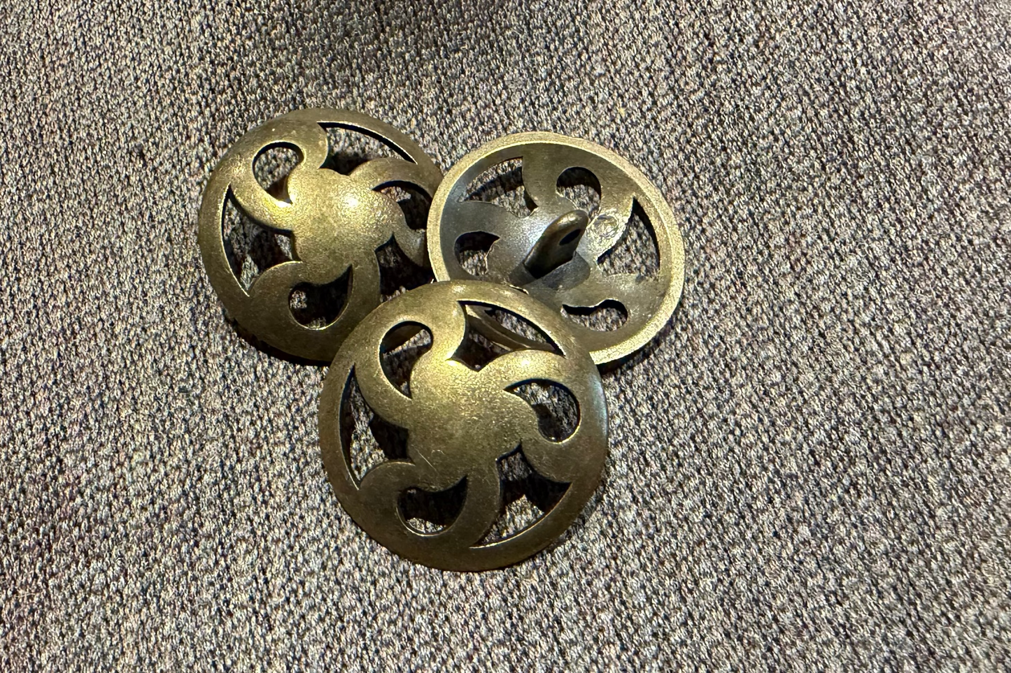 Three gold buttons with intricate designs on a textured gray surface