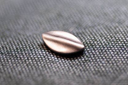 Metallic teardrop-shaped button on a textured gray surface